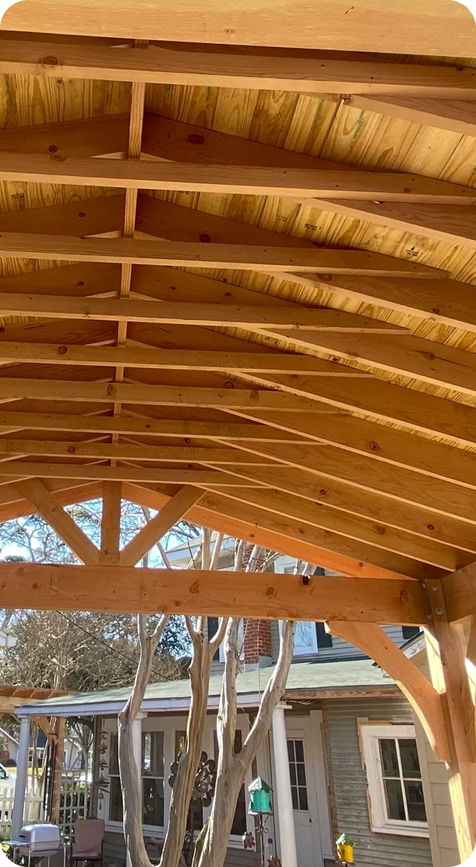 Wooden pergola roof with house in background.