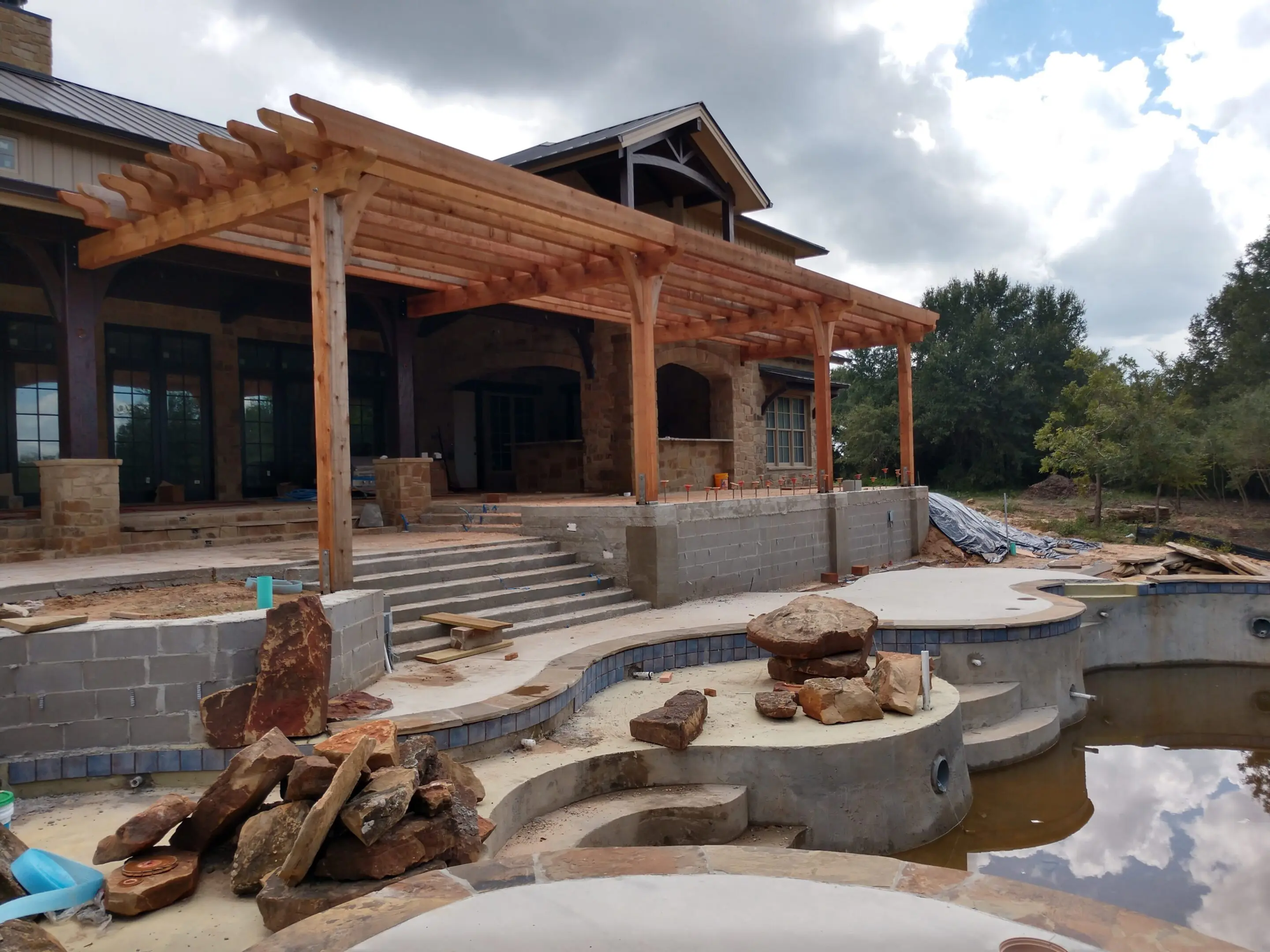 Outdoor patio with a wooden pergola and stone steps under construction.