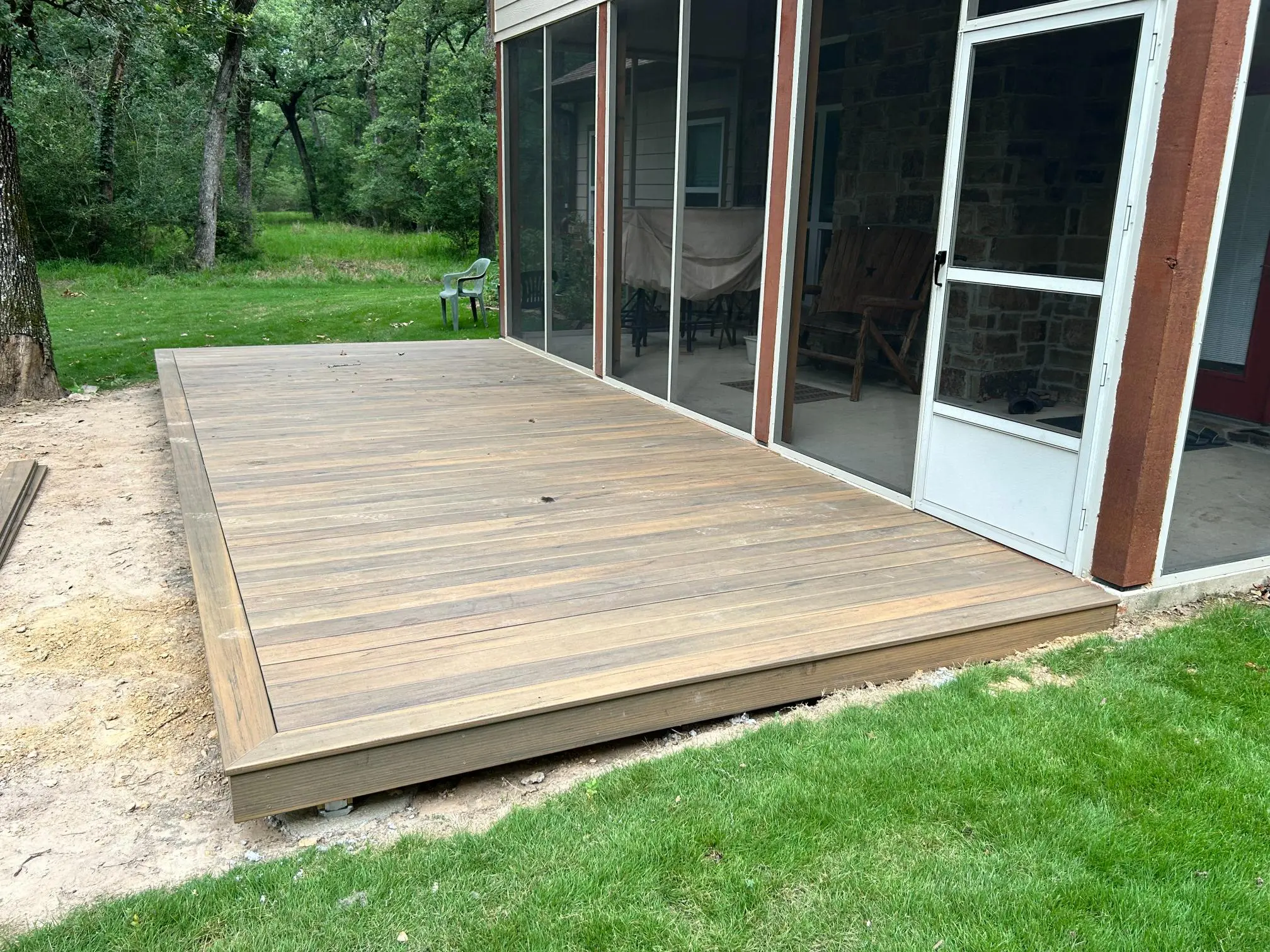 New wooden deck attached to a house with screened porch.