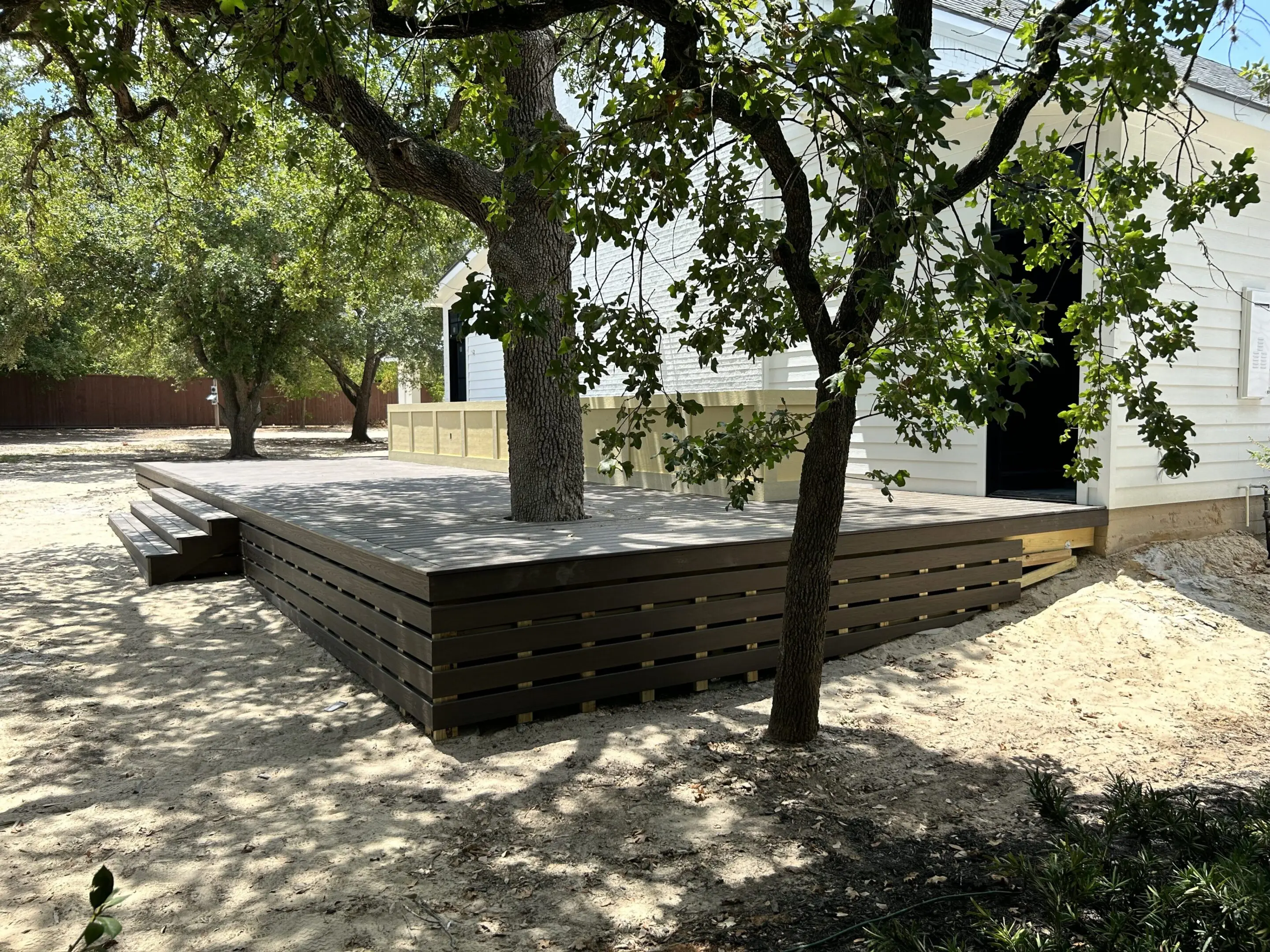 A large rectangular stone bench under trees in a shaded park area.