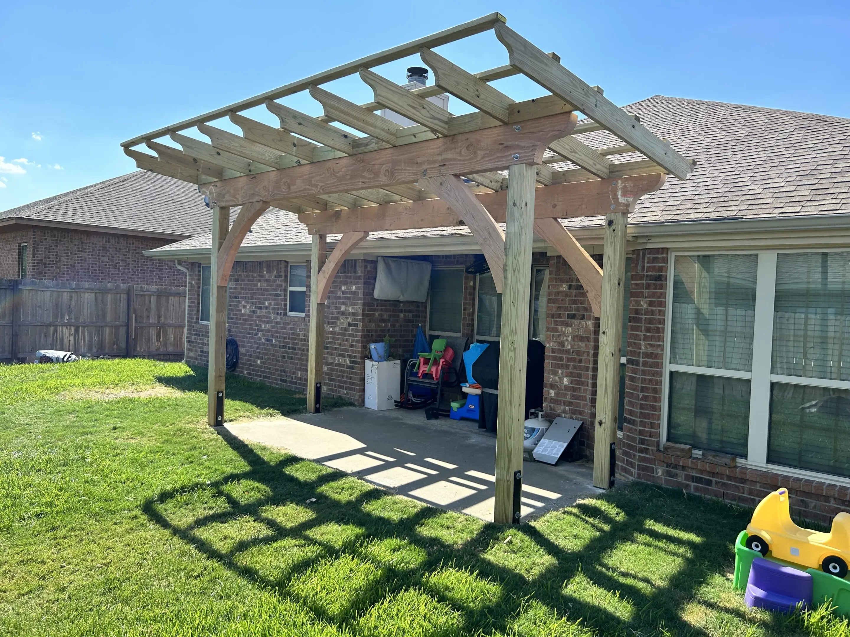 A wooden pergola casting shadows on a backyard patio.