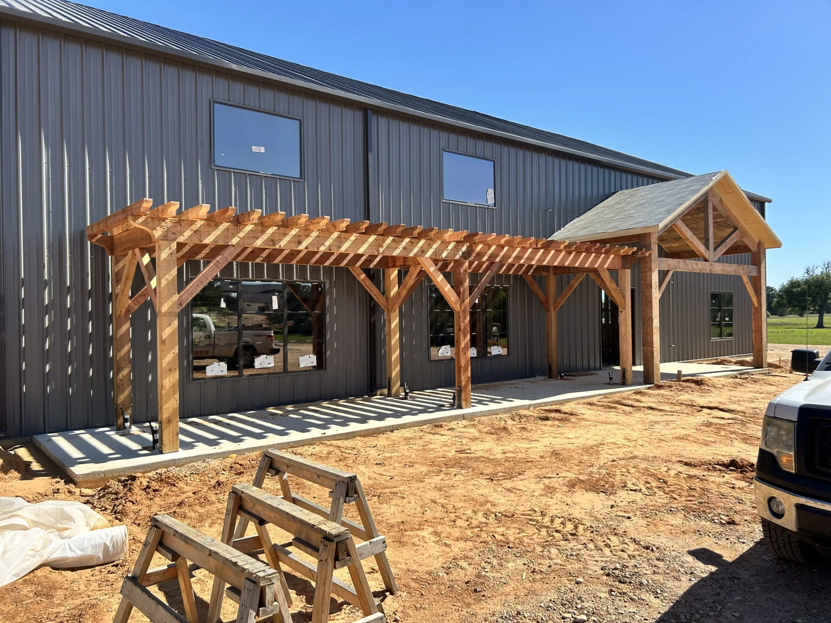 A modern barn with a wooden pergola under construction in front.