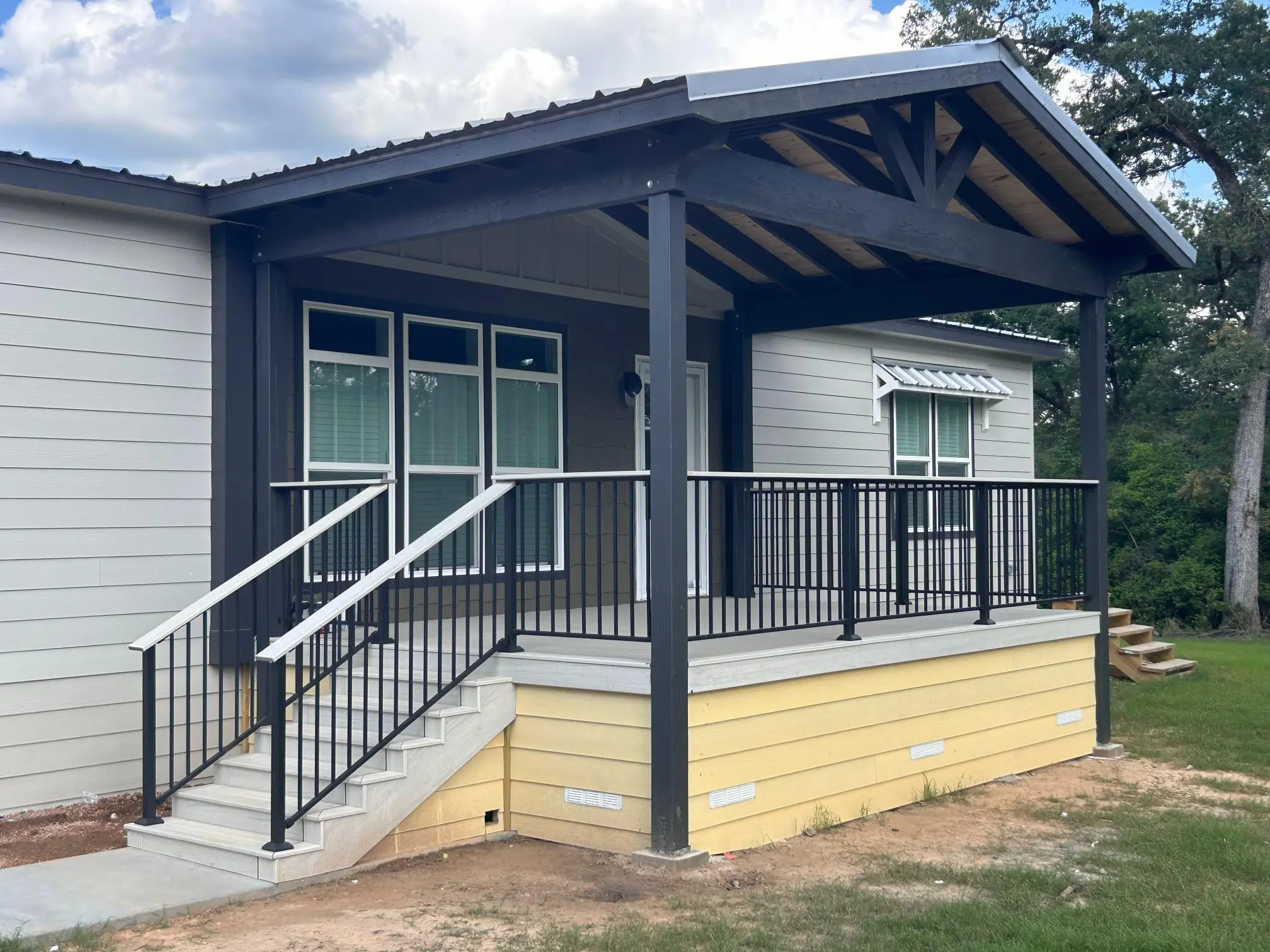 Newly built porch with black railing and beige siding on a house.