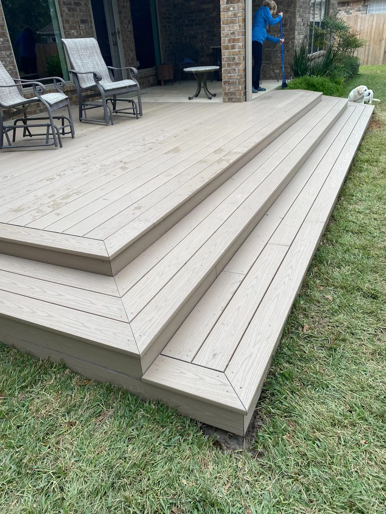 Wide wooden steps leading up to a deck in a backyard.