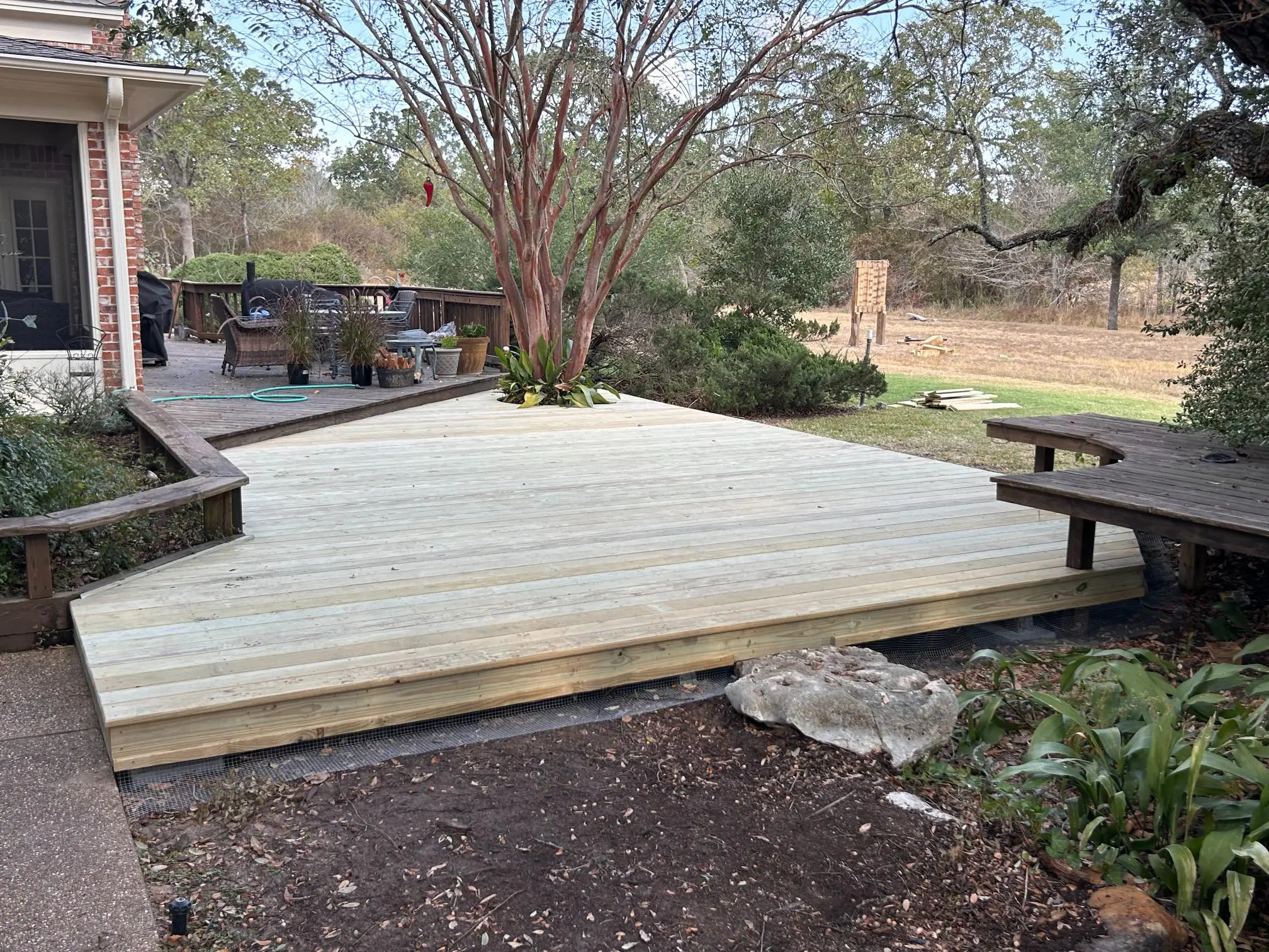 New wooden deck built in a backyard with benches and trees.