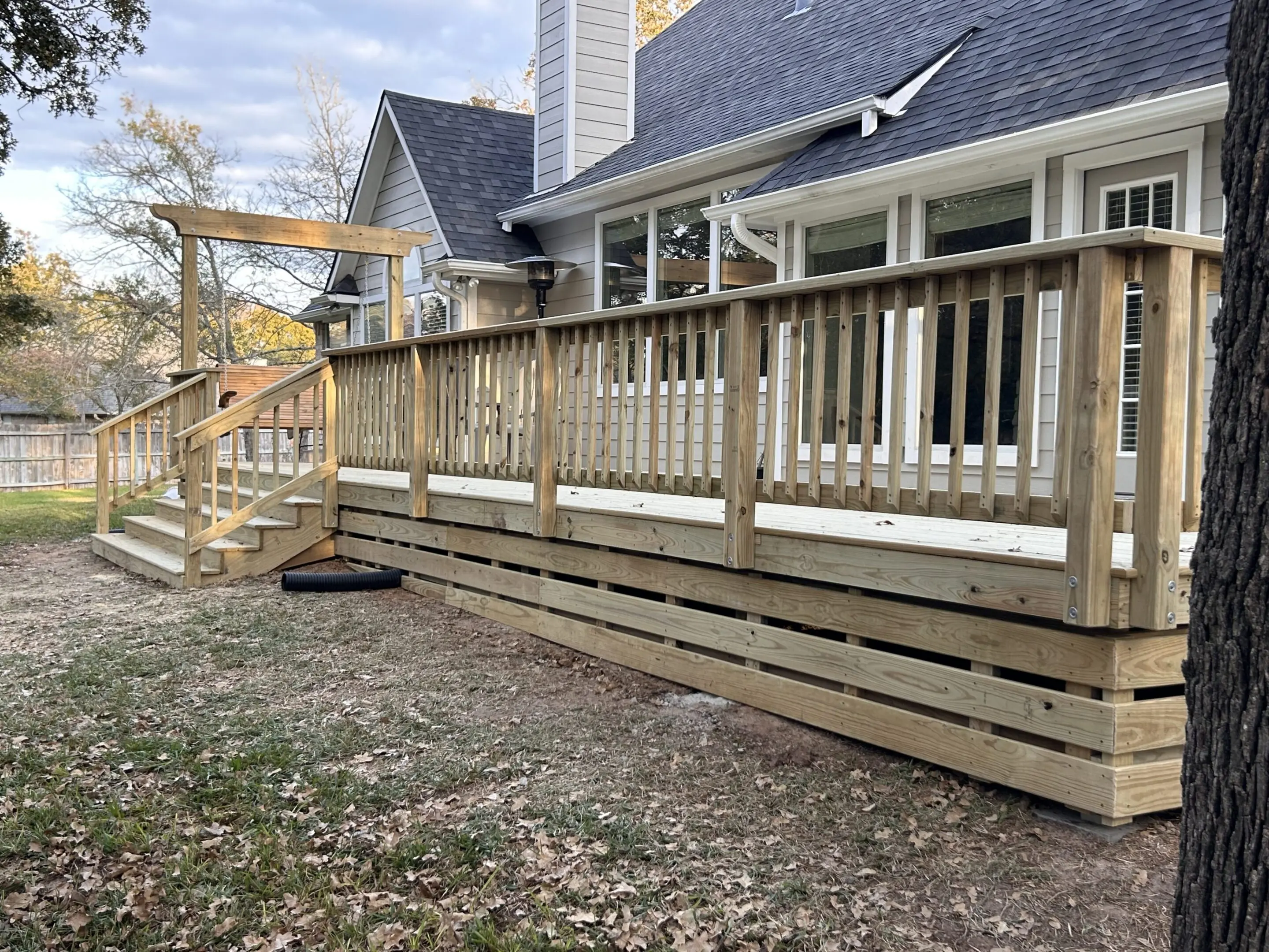 Wooden deck railing with a decorative design in front of a house.