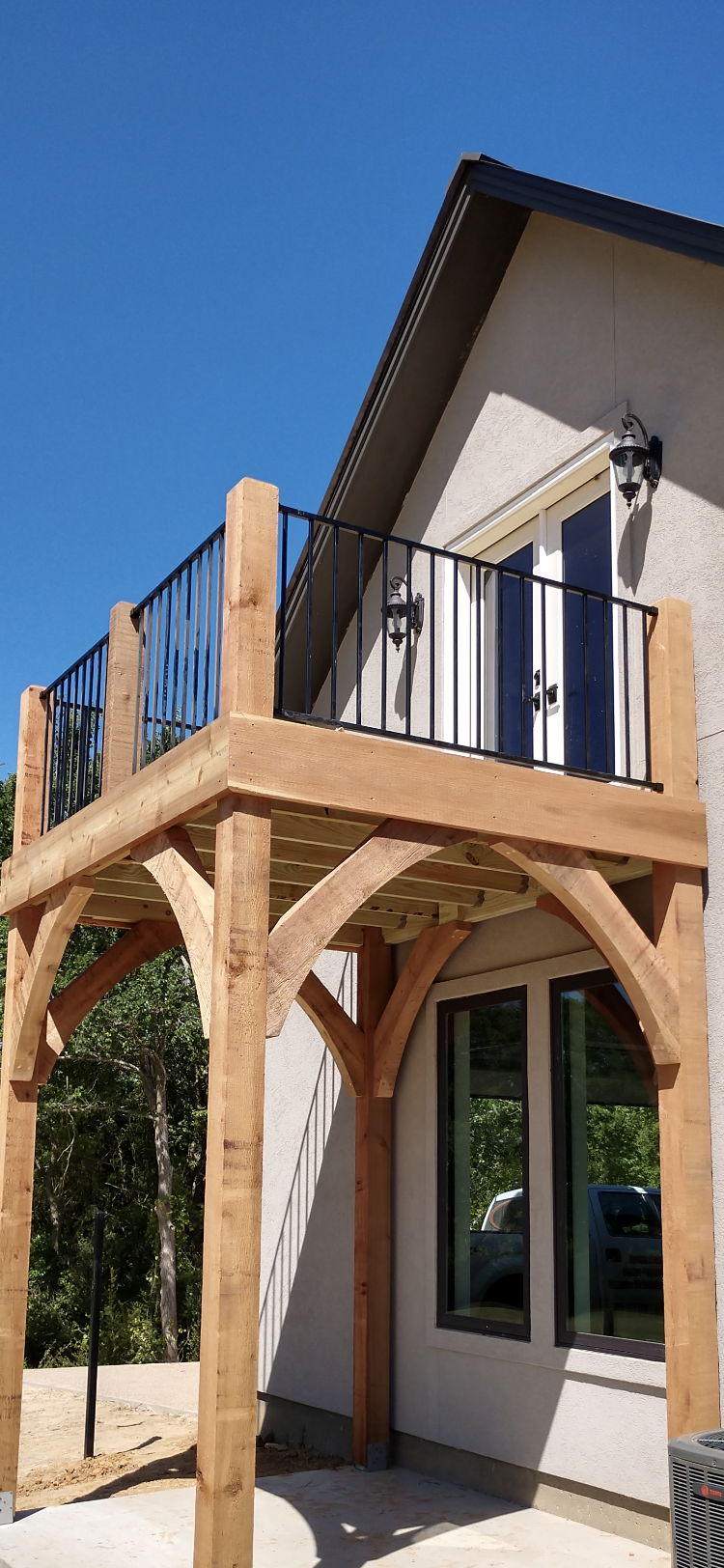 Wooden balcony with black metal railing attached to a house.