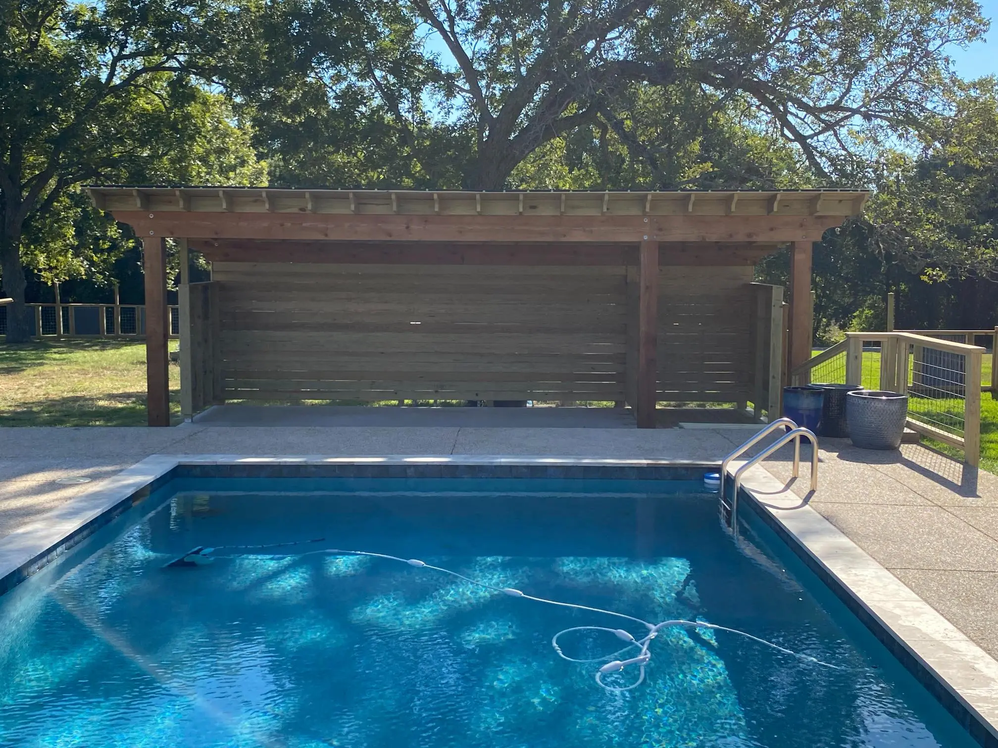 A serene backyard pool with a wooden pergola and lounge chairs.