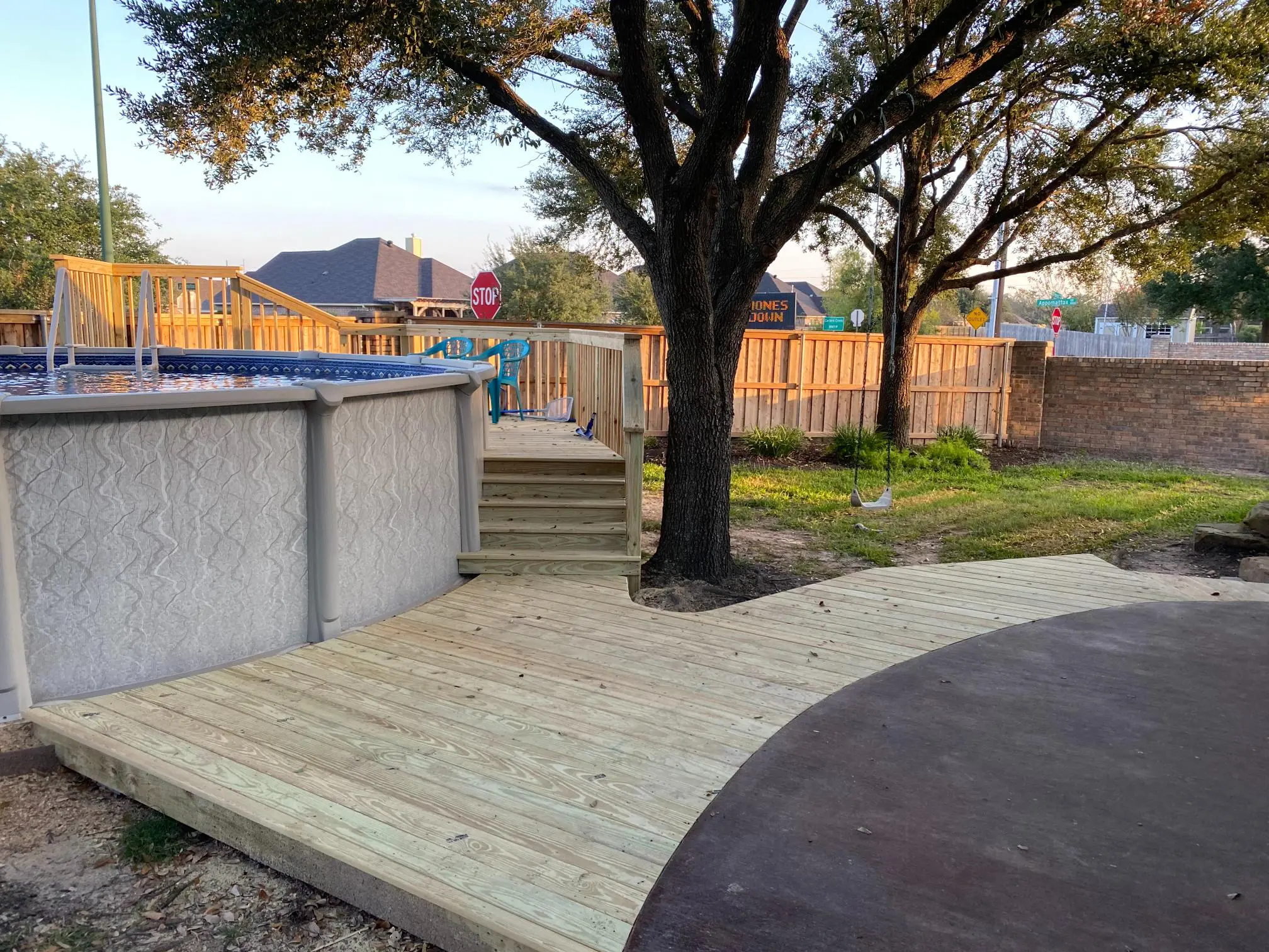 A backyard with an above-ground pool, wooden deck, and a large tree.