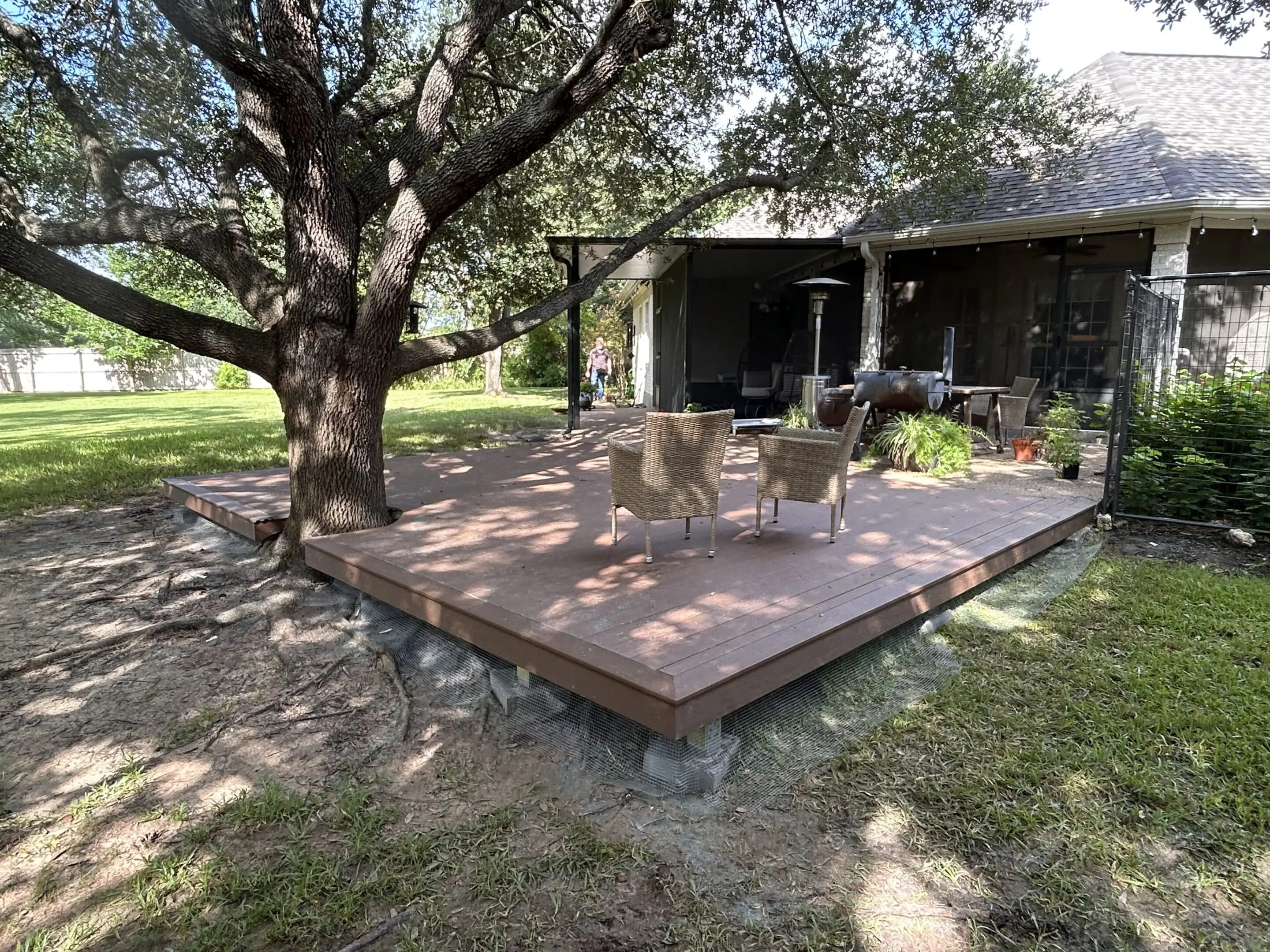 A wooden deck with outdoor furniture under a large tree.