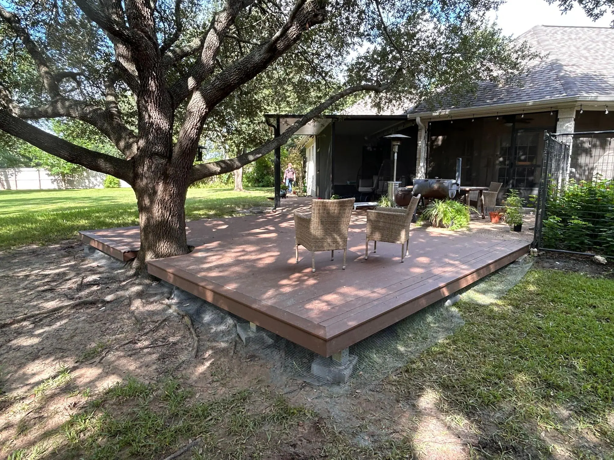 Wooden deck with outdoor furniture under a large tree in a backyard.
