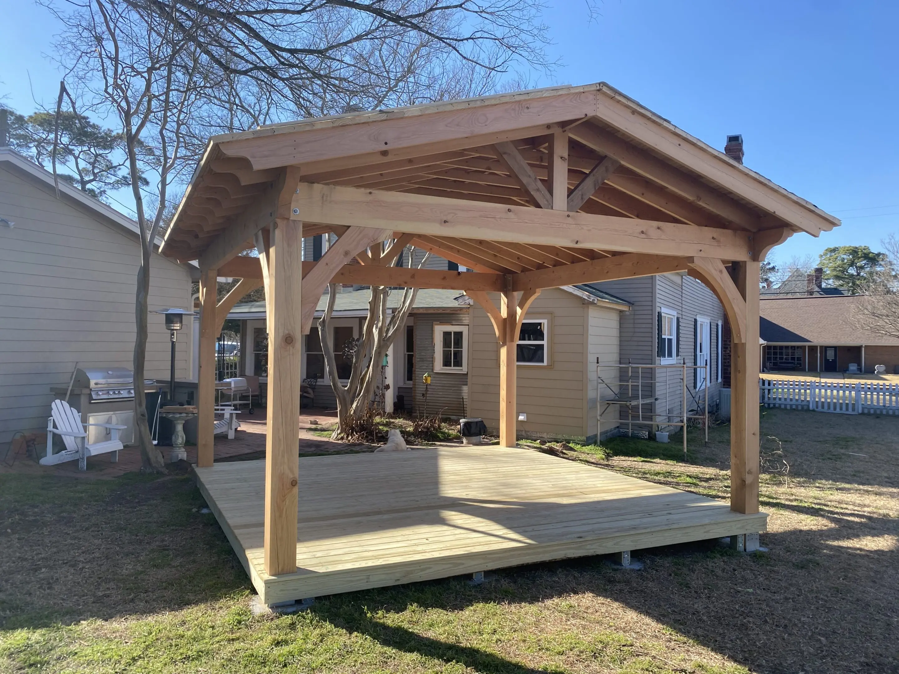 Wooden gazebo structure in a backyard under clear blue sky.