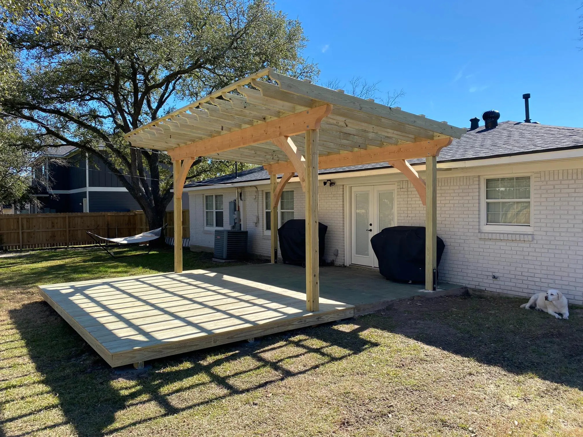 Wooden pergola structure in a backyard casting shadows on grass.