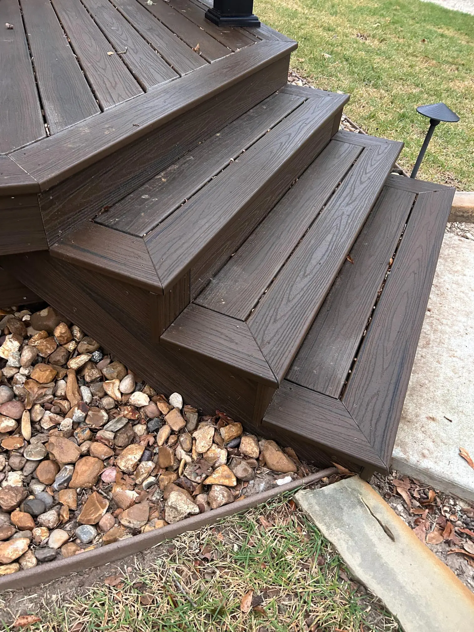 Dark brown wooden stairs with stone ground cover beneath.