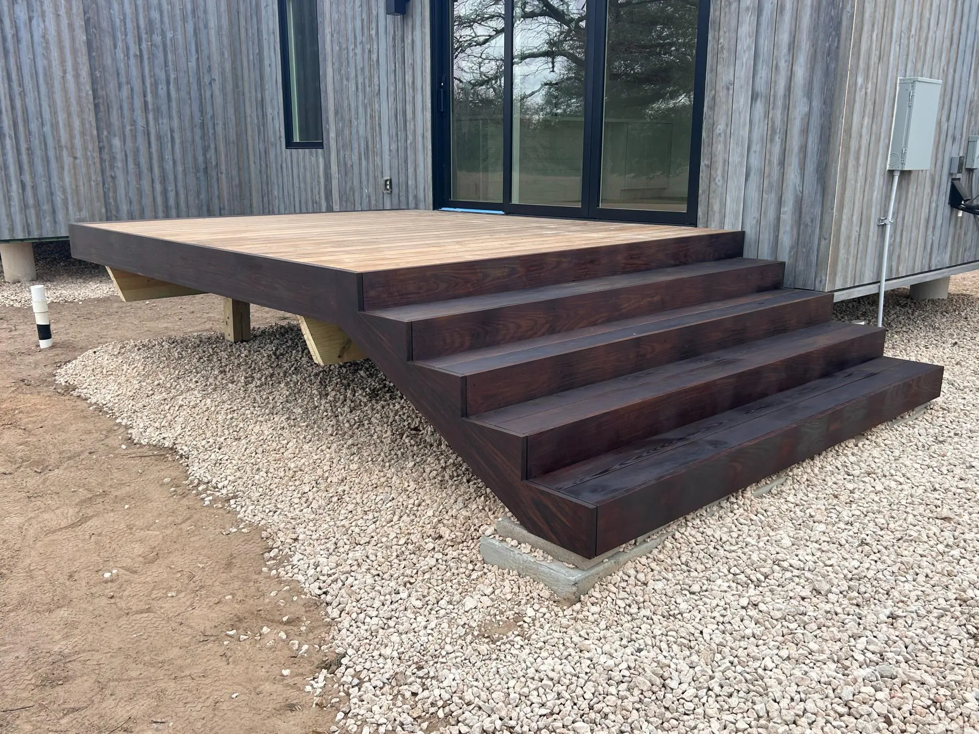 Modern wooden deck with built-in stairs and gravel base.