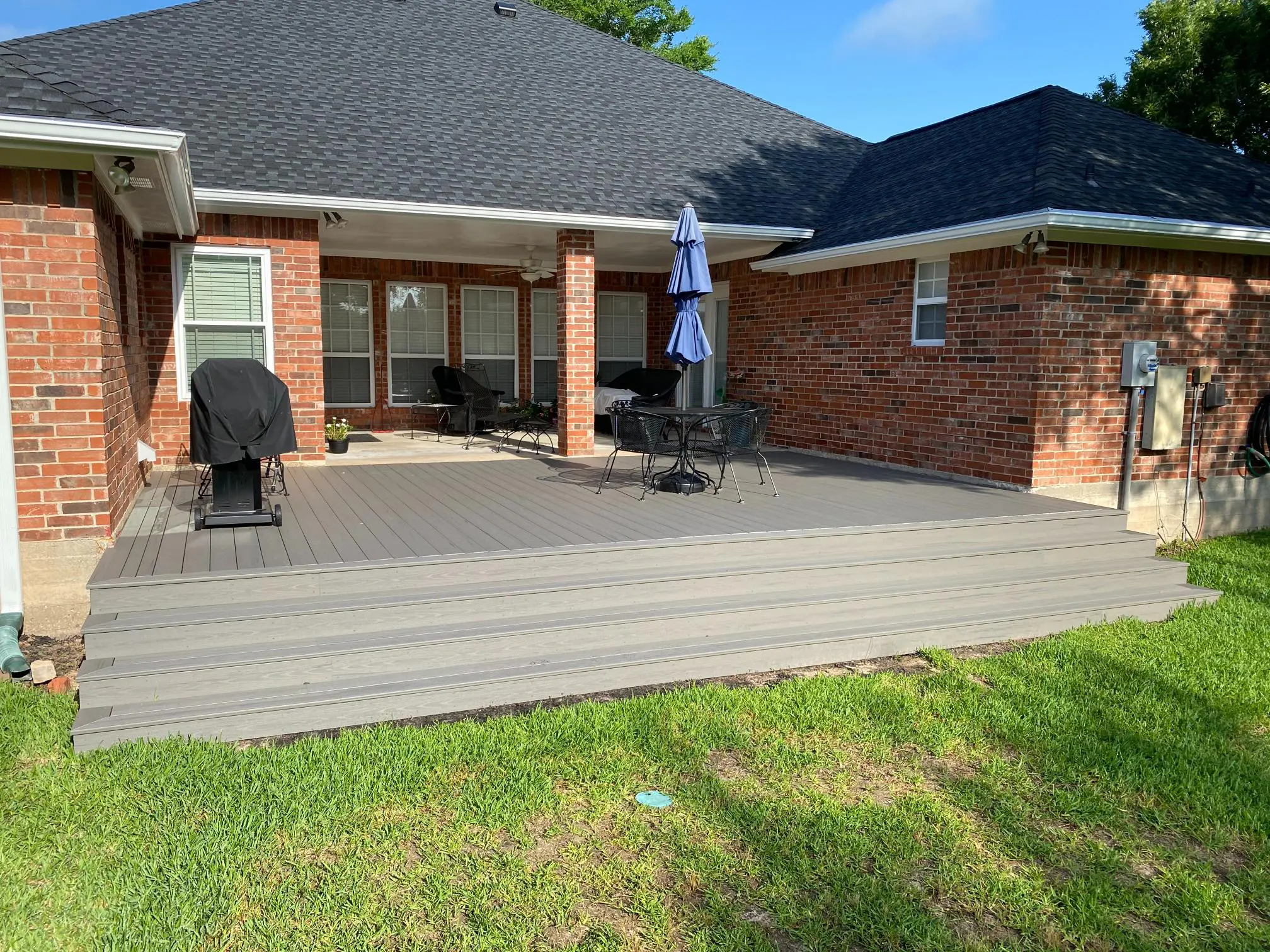 A backyard patio with a grill, table, and umbrella on a sunny day.