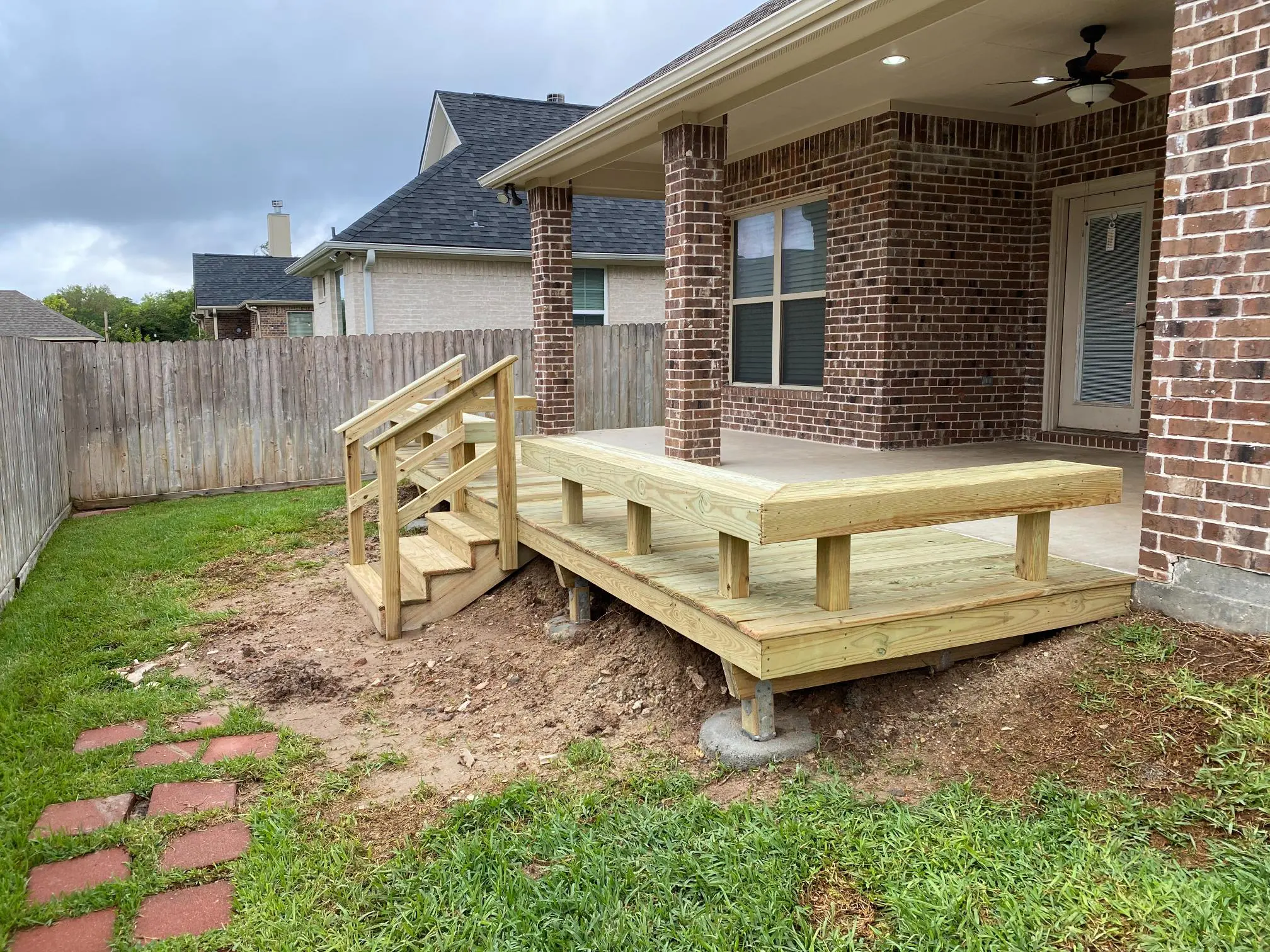 New wooden deck with stairs next to a brick house.