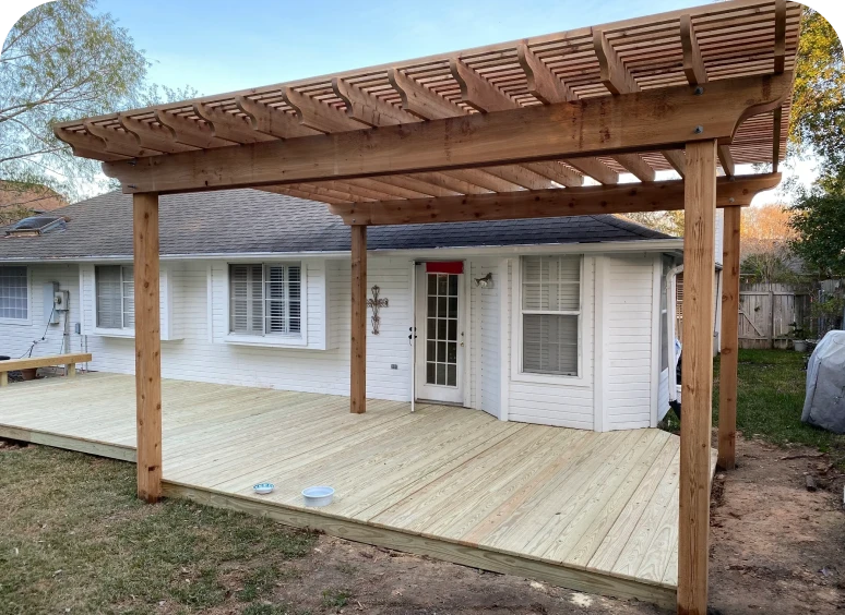 Wooden pergola over backyard deck, white house.
