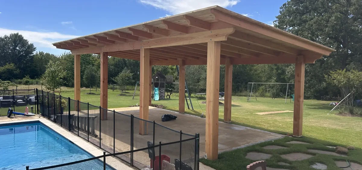 Wooden pergola structure in a backyard with a grassy area and play equipment.